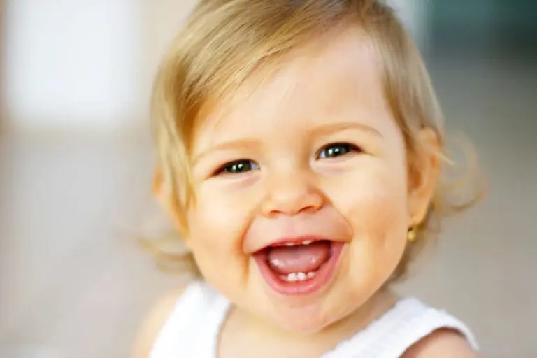A smiling baby in a white top and gold earring looks at the camera at Lake Sammamish Kids Dentistry in Sammamish, WA.