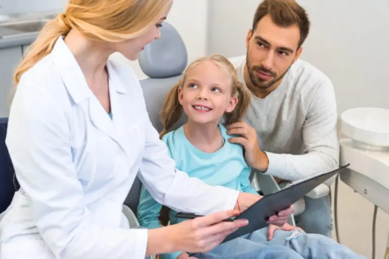 At Lake Sammamish Kids Dentistry in Sammamish, WA, a female dentist shows a clipboard to a young girl with her father beside her - Best Toothbrush for Kids by Age – Sammamish Parent Guide