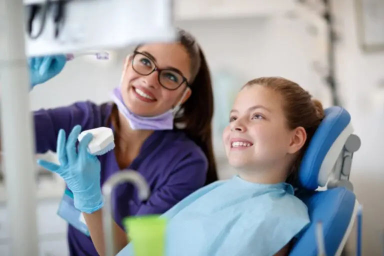 At Lake Sammamish Kids Dentistry in Sammamish, WA, a dentist shows a tooth model to a smiling child in the dental chair - School Dental Health Programs in Sammamish, WA