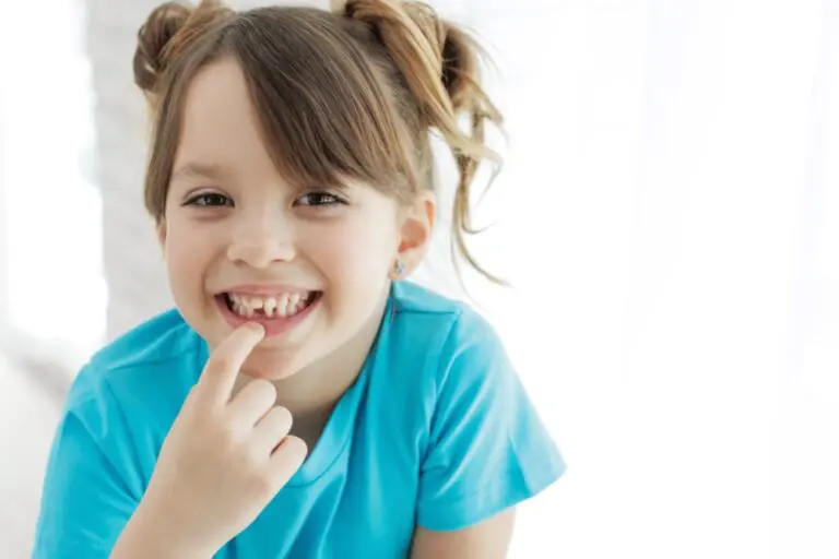 A smiling young girl in a blue shirt points to her missing tooth at Lake Sammamish Kids Dentistry in Sammamish, WA - Jaw Alignment Issues in Kids: Signs to Watch for in Sammamish, WA