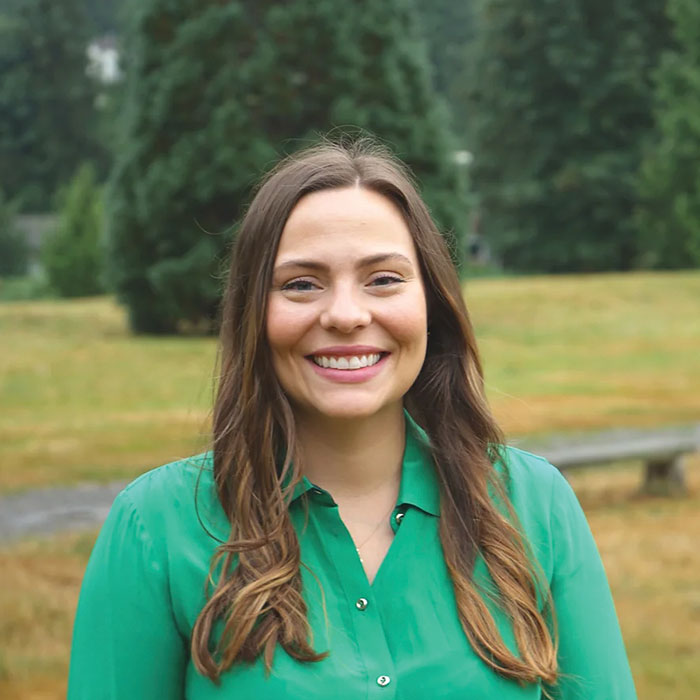At Lake Sammamish Kids Dentistry - Pediatric Dentist in Sammamish WA, Dr. Annikka Freelove, DDS, a board-certified pediatric dentist with long brown hair and a green blouse, smiles outdoors amid trees and grass.