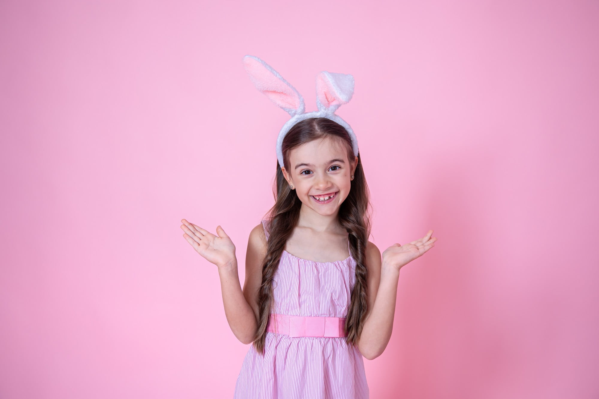 A young girl in bunny ears and a pink dress smiles playfully against a pink background—an ideal image to promote Lake Sammamish Kids Dentistry - Pediatric Dentist in Sammamish WA, highlighting their safe sedation dentistry in a child-friendly atmosphere.