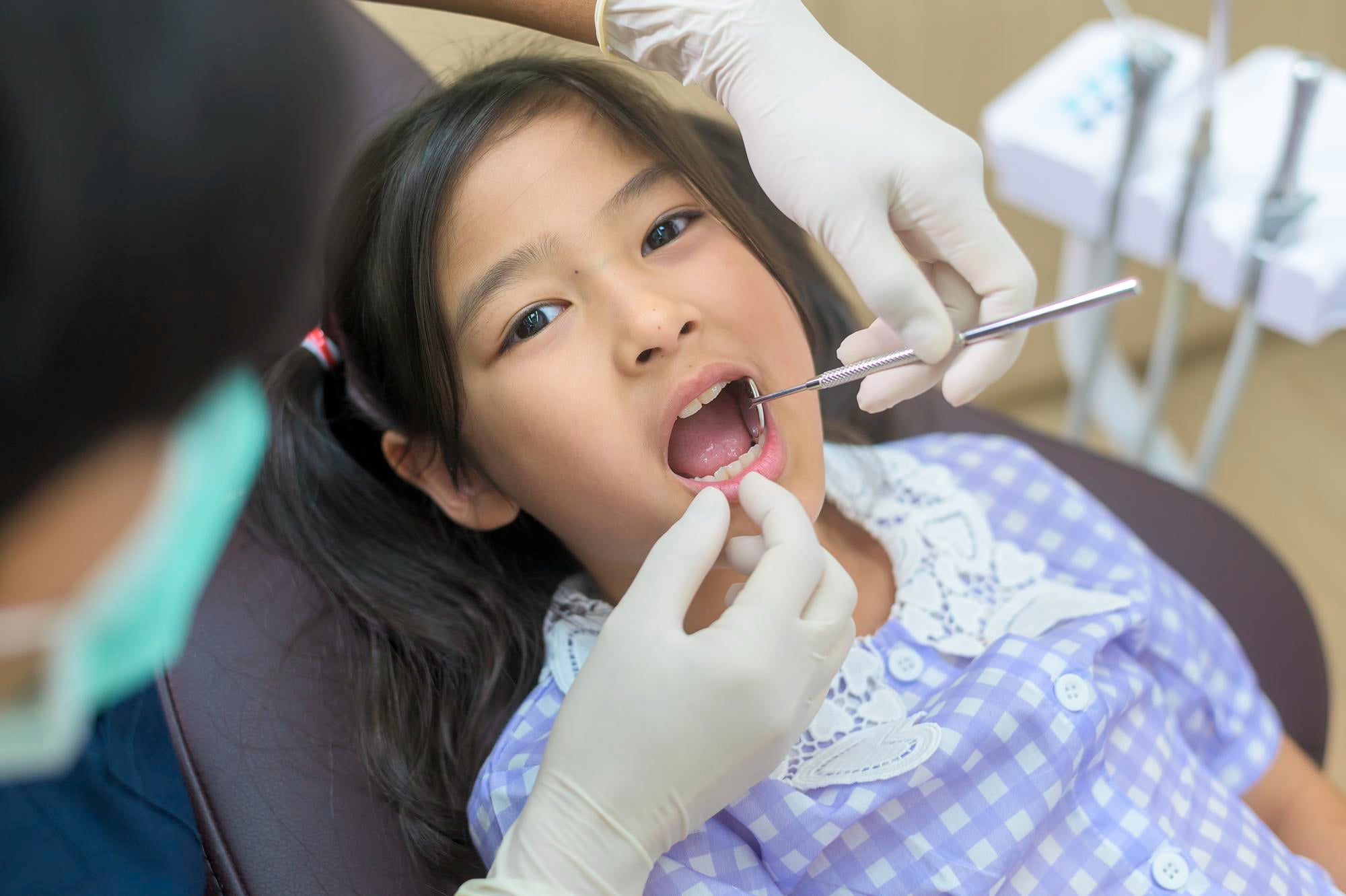 At Lake Sammamish Kids Dentistry - Pediatric Dentist in Sammamish WA, a young girl in a purple and white dress sits in the dental chair while the dentist examines her teeth, demonstrating the value of restorative dentistry for children and tooth-colored fillings for a natural look.