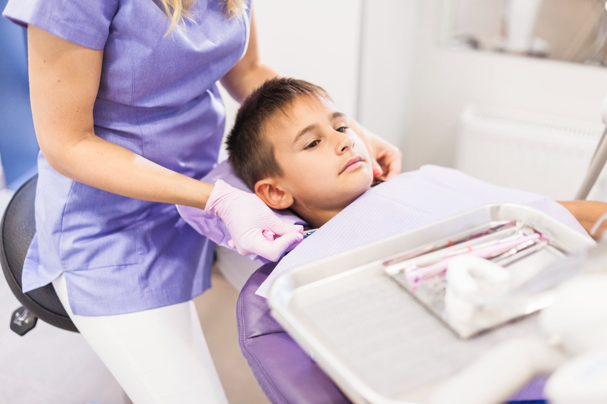 At Lake Sammamish Kids Dentistry - Pediatric Dentist in Sammamish WA, a board-certified dental professional adjusts a protective apron on a young boy in the dental chair, ensuring strict safety protocols are followed while dental instruments rest on a nearby tray.