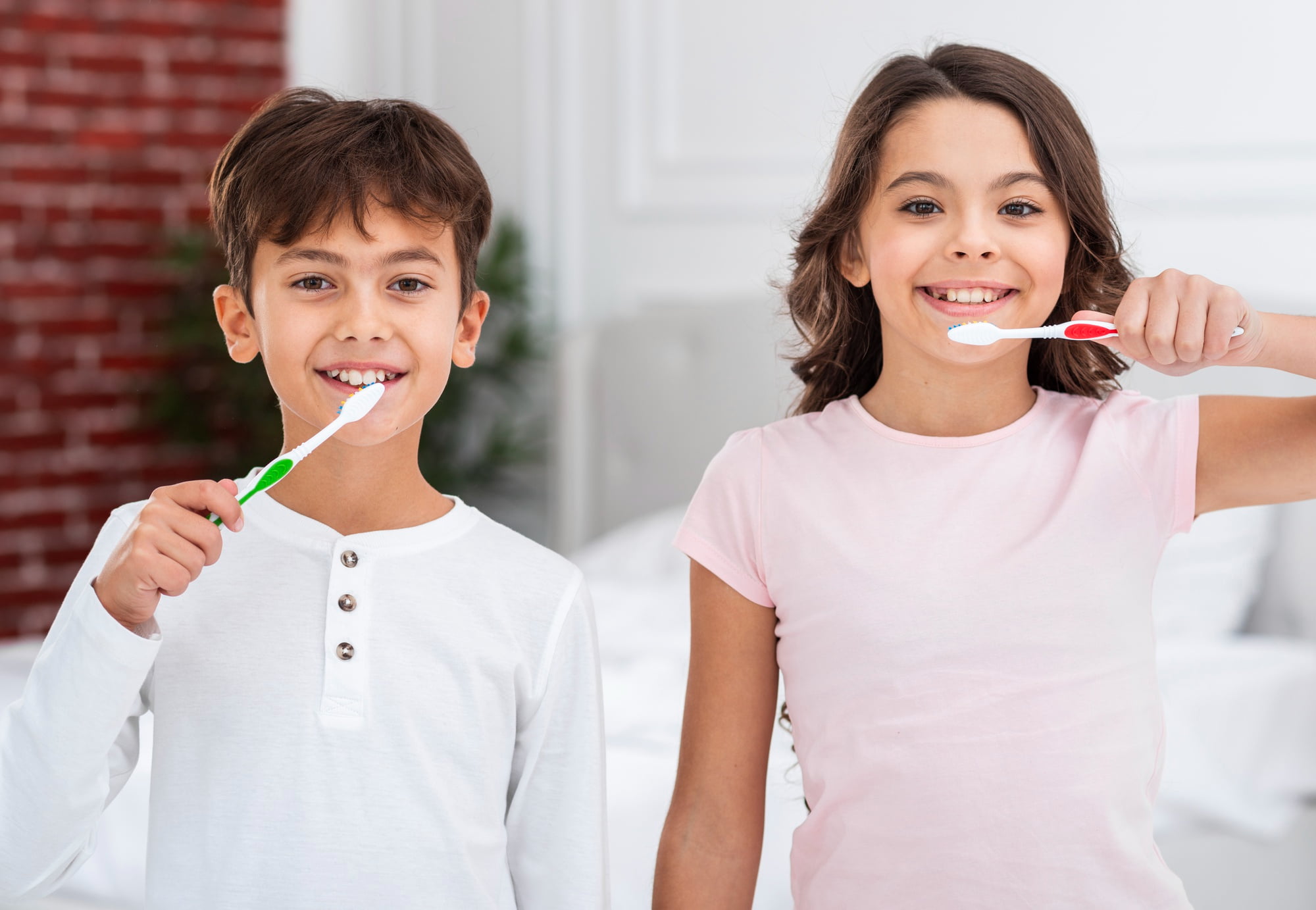 At Lake Sammamish Kids Dentistry - Pediatric Dentist in Sammamish WA, two smiling children brush their teeth indoors with toothbrushes, promoting healthy habits inspired by the ABCD Program offering free dental care for kids six and under.