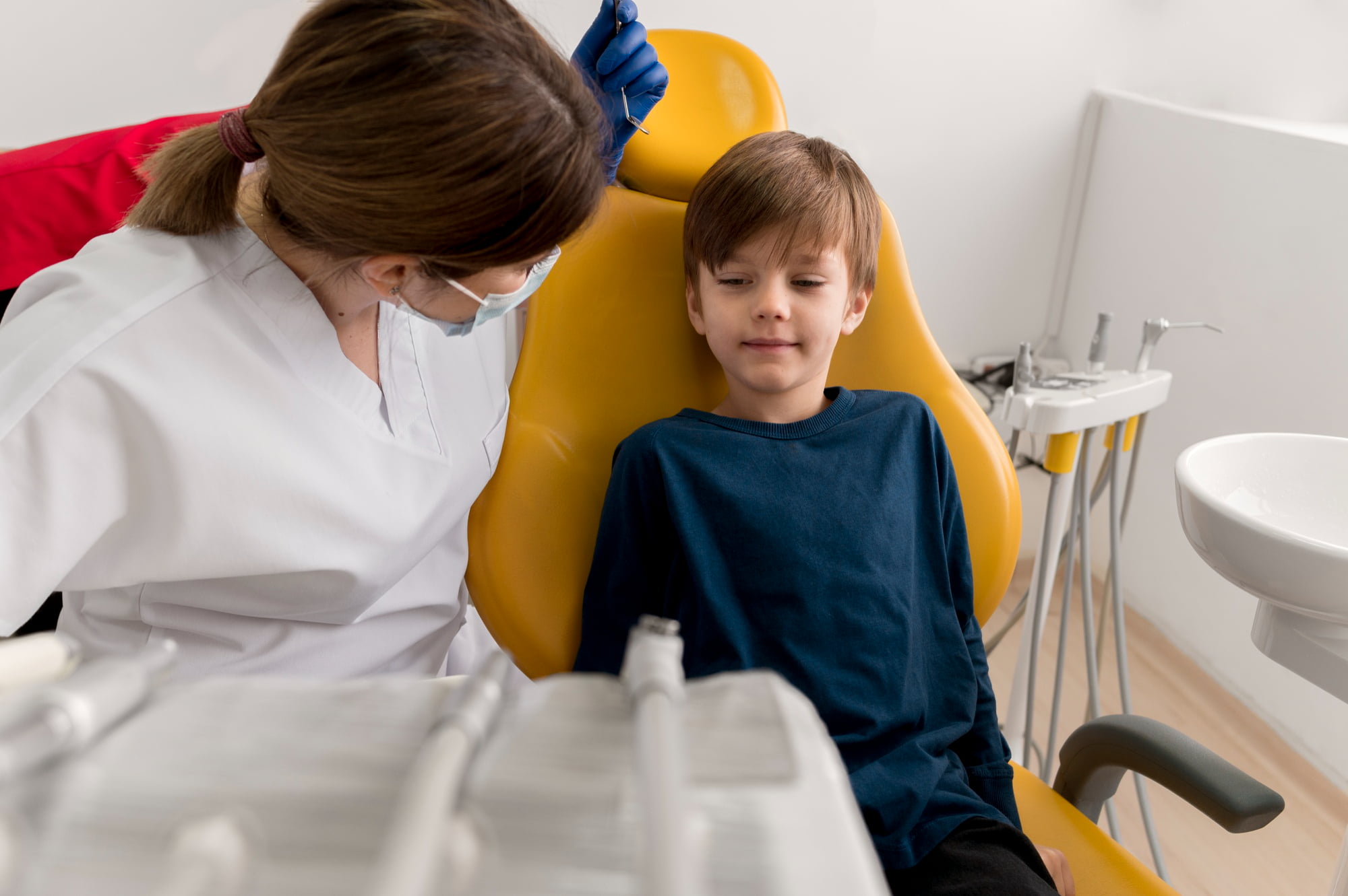 At Lake Sammamish Kids Dentistry - Pediatric Dentist in Sammamish WA, a dentist wearing a mask and gloves consults with a young boy seated in a yellow dental chair; the clinic provides flexible scheduling for special-needs families.