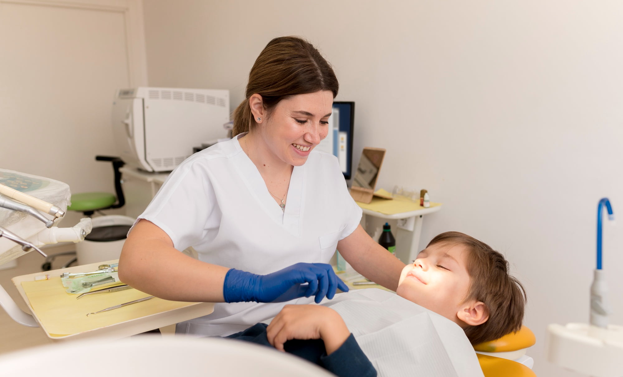 At Lake Sammamish Kids Dentistry - Pediatric Dentist in Sammamish WA, a dentist skilled in behavioral management and communication techniques examines a smiling young boy reclining in a brightly lit clinic.