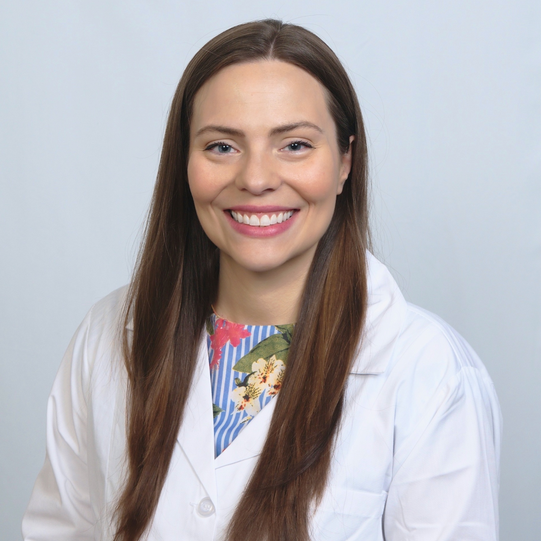At Lake Sammamish Kids Dentistry - Pediatric Dentist in Sammamish WA, Dr. Annikka Freelove, DDS—board-certified pediatric dentist—smiles at the camera, wearing a white lab coat over a floral top with her long brown hair against a light background.