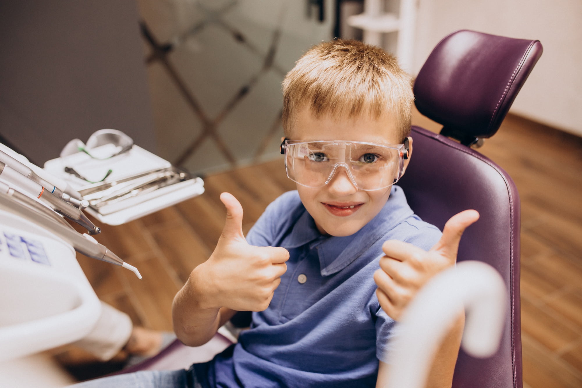 At Lake Sammamish Kids Dentistry - Pediatric Dentist in Sammamish WA, a young boy wearing safety glasses sits in the dental chair and gives two thumbs up, illustrating how reduced anxiety leads to more smiles at every visit.
