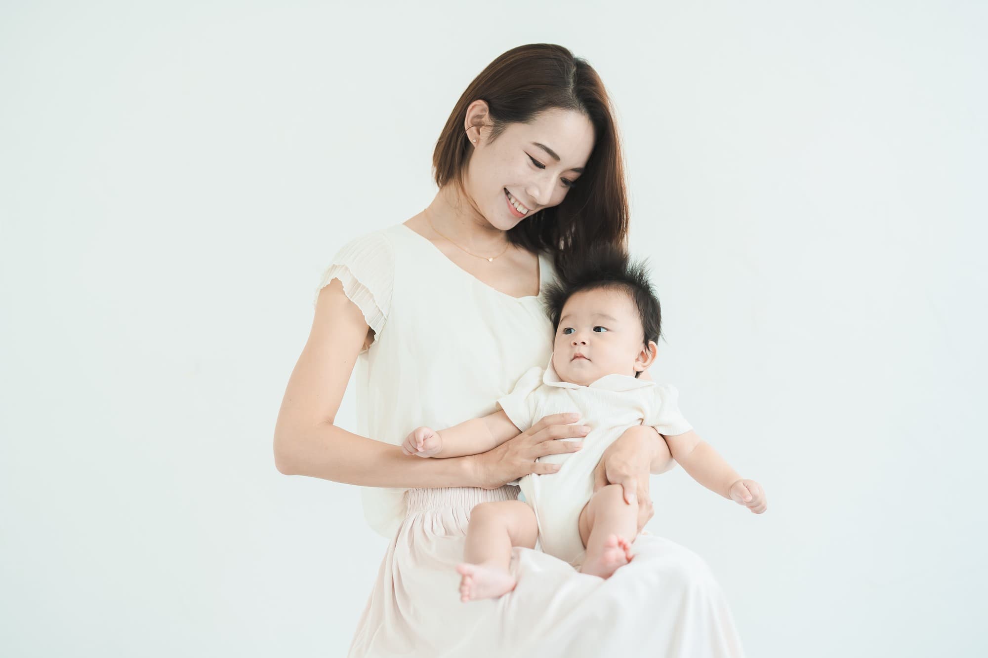 An ideal image for illustrating Baby Dentist Parent Education & Home-Care Tips at Lake Sammamish Kids Dentistry - Pediatric Dentist in Sammamish, WA features a woman and baby, both dressed in white, facing the camera against a plain white background.