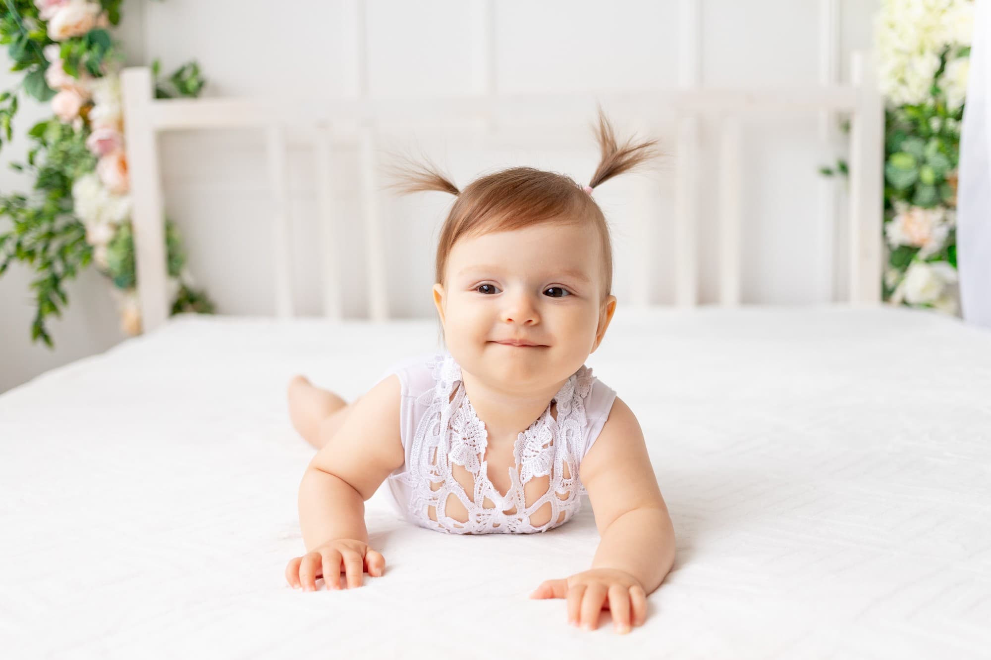 Learn about Baby Dentist Thumb-Sucking & Pacifier Guidance at Lake Sammamish Kids Dentistry - Pediatric Dentist in Sammamish WA, with this image of a baby in white lace, lying on a bed with light brown hair in pigtails and a calm expression.