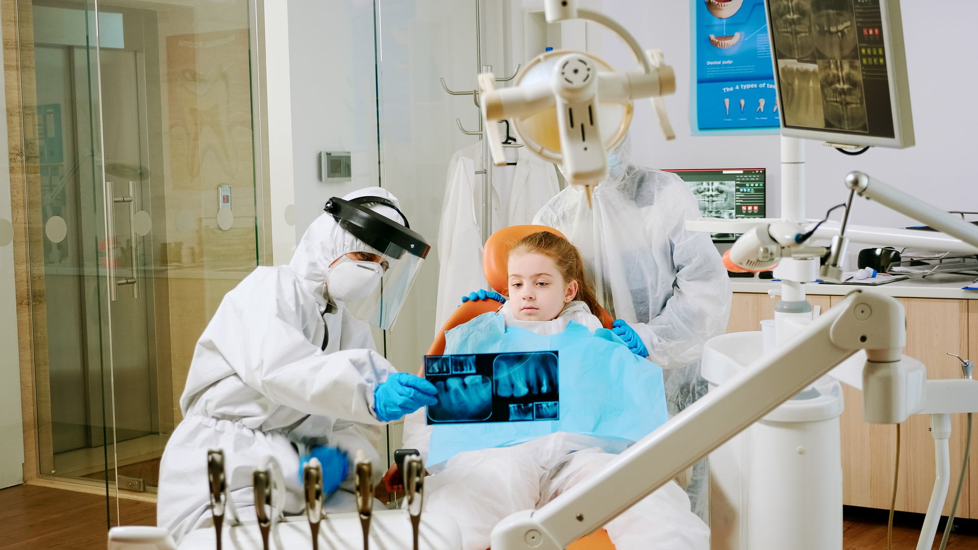 At Lake Sammamish Kids Dentistry - Pediatric Dentist in Sammamish WA, a child sits in a modern clinic's dental chair as professionals in protective gear use advanced technology to show her dental X-rays.