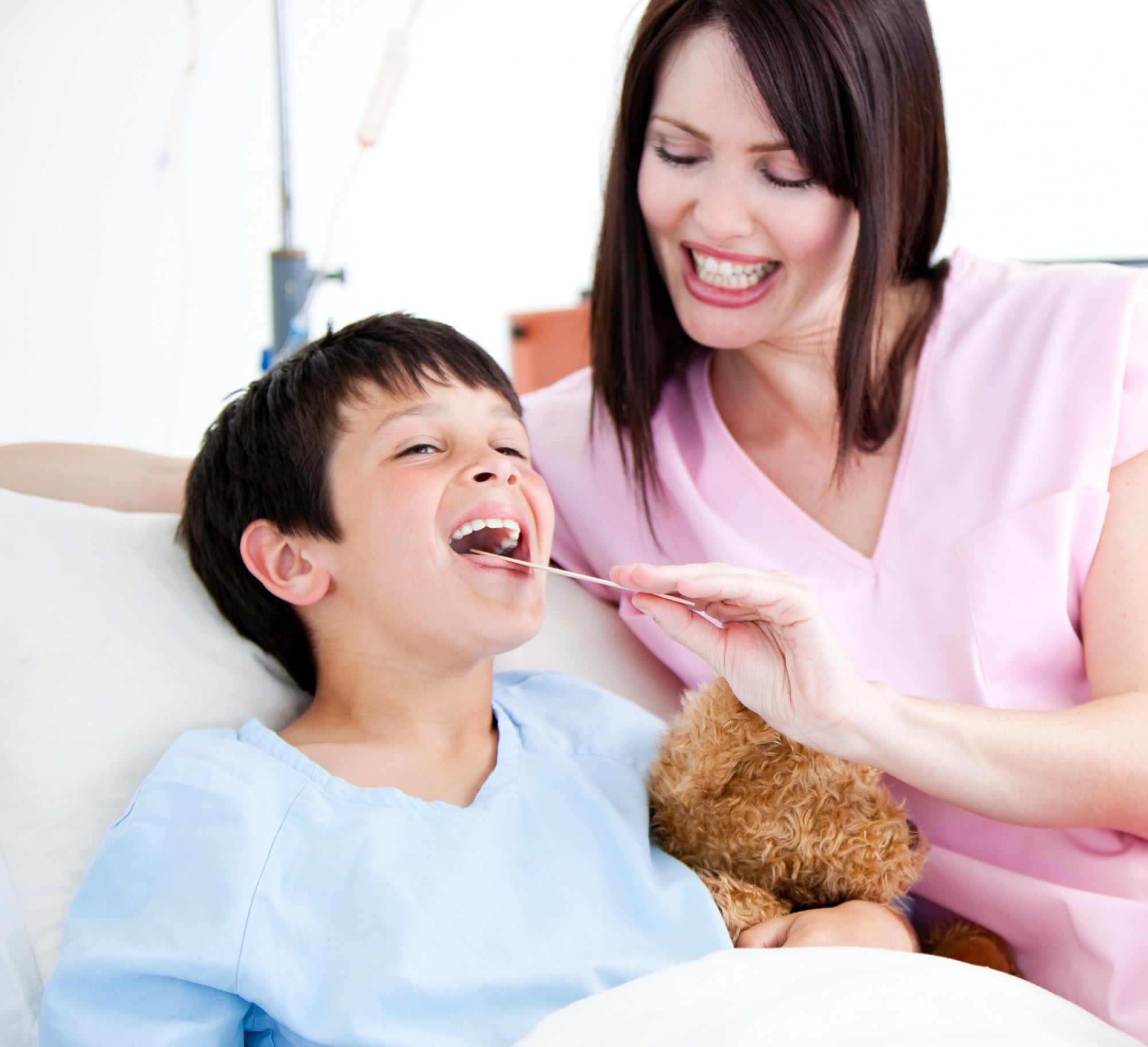 At Lake Sammamish Kids Dentistry - Pediatric Dentist in Sammamish WA, hospital general anesthesia is provided when medically necessary, such as when a healthcare professional examines a child—like a young boy holding a teddy bear—as seen during throat checks with a tongue depressor.