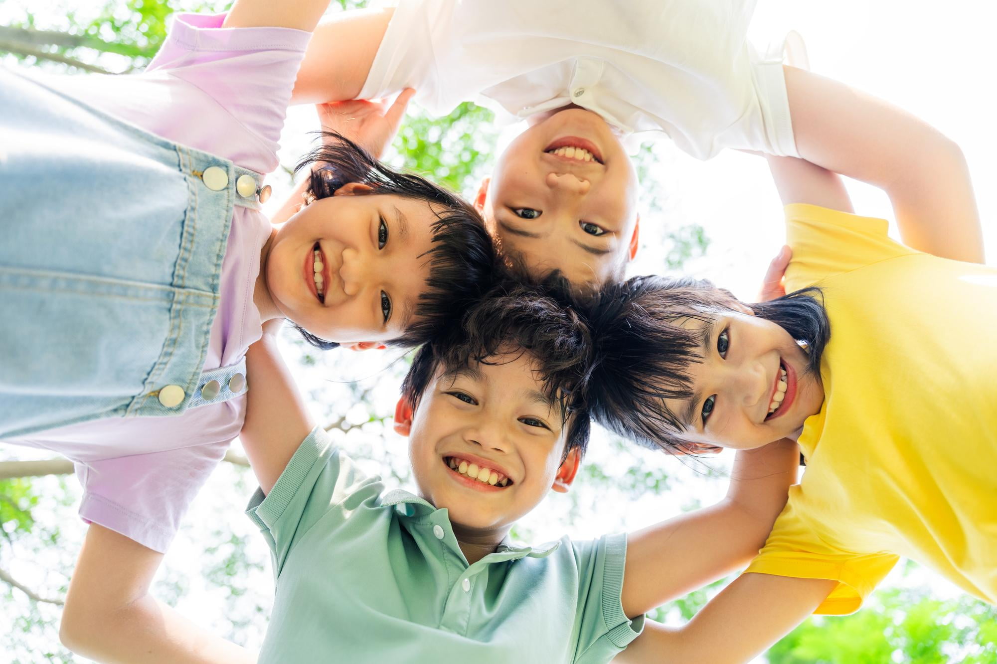 Four children stand outdoors in a circle, smiling down at the camera with arms around each other’s shoulders—showcasing bright smiles thanks to Lake Sammamish Kids Dentistry - Pediatric Dentist in Sammamish, WA.