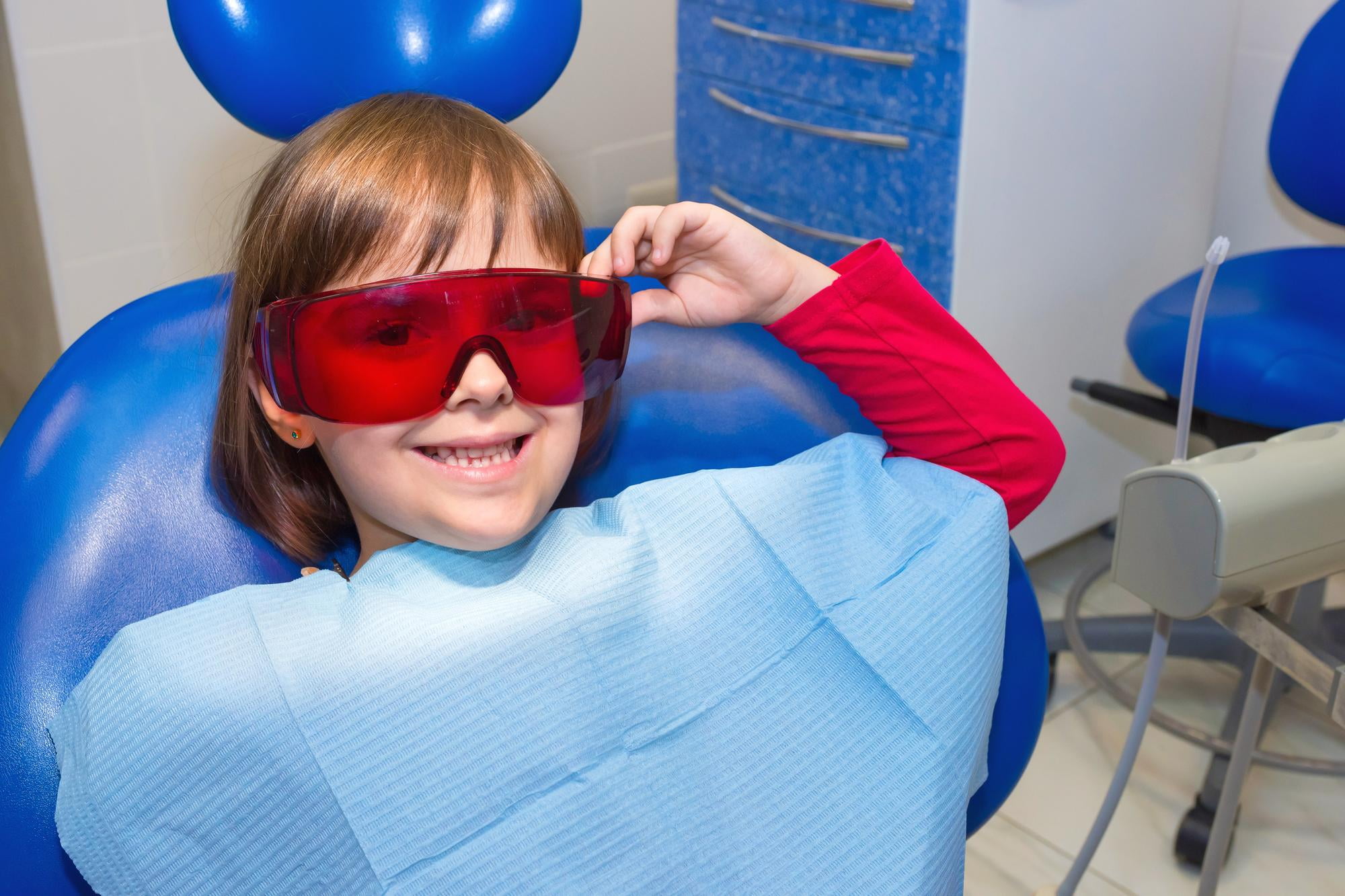 At Lake Sammamish Kids Dentistry - Pediatric Dentist in Sammamish WA, a young child sits in the dental chair wearing a bib and red protective glasses, smiling confidently and ready to go back to school the same day with a bright, healthy smile.