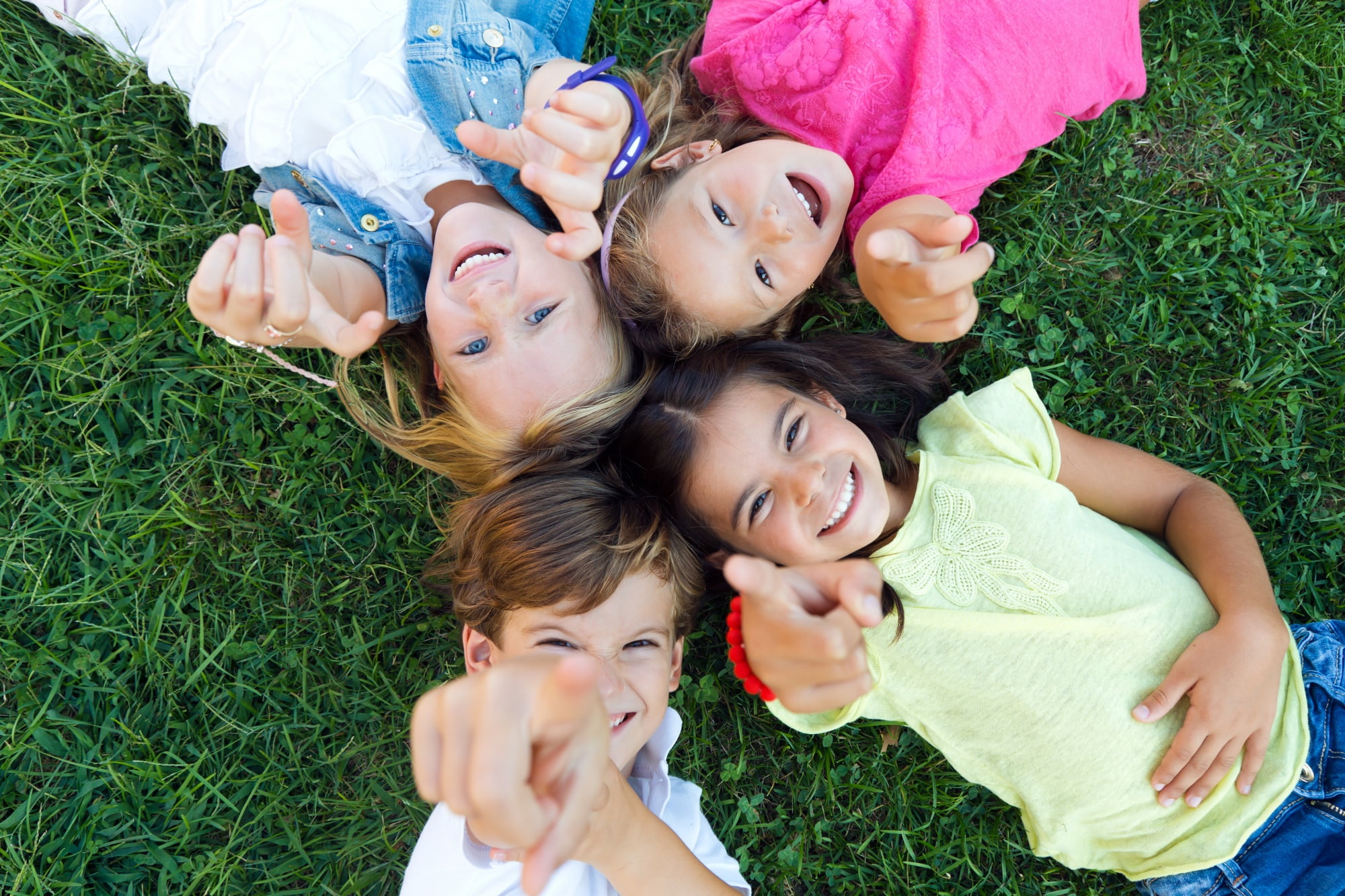 Smiling and pointing towards the camera, four children lie on the grass in a circle—perfect moments cared for by Lake Sammamish Kids Dentistry - Pediatric Dentist in Sammamish, WA. Schedule your appointment today!.