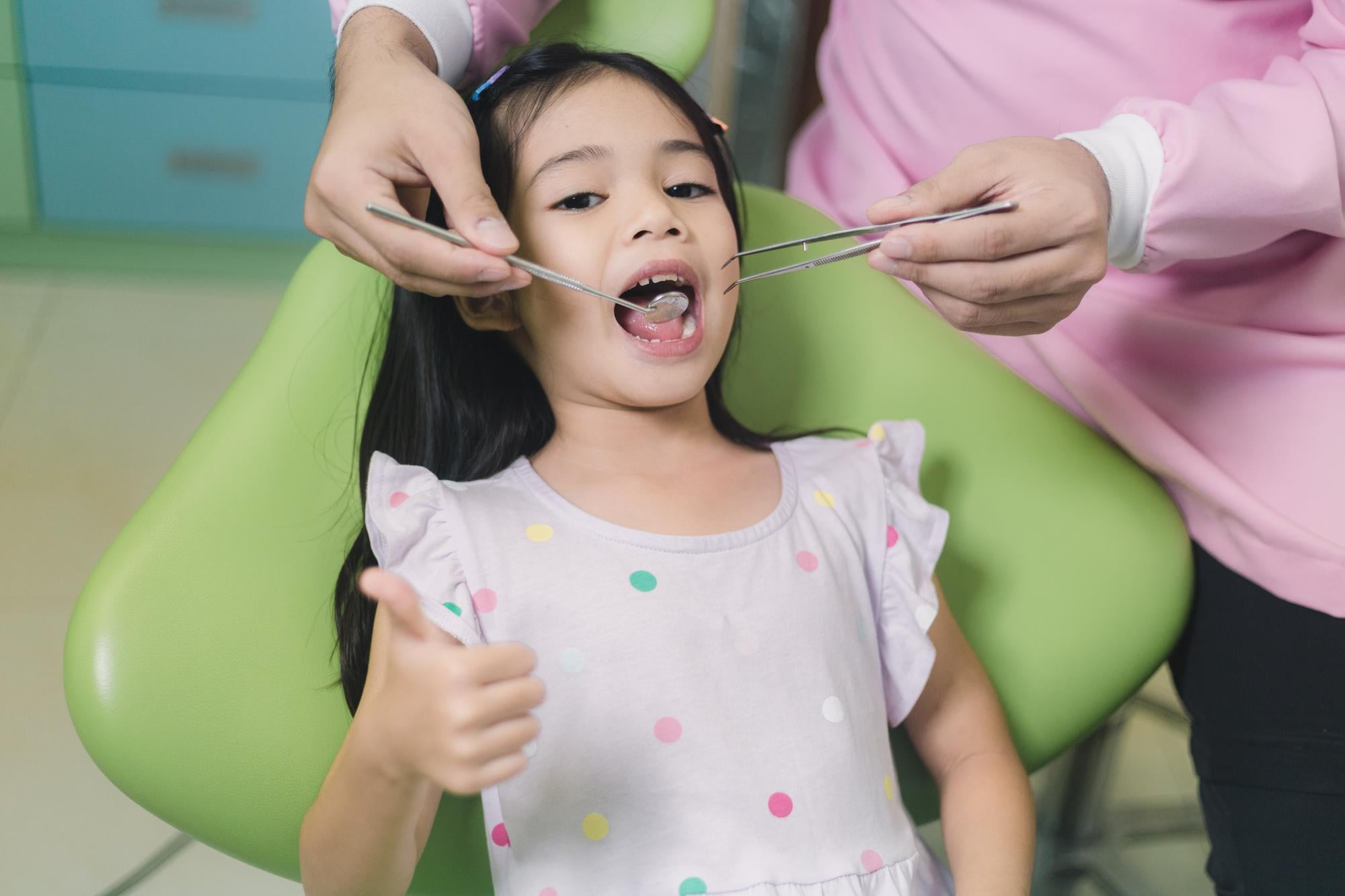 At Lake Sammamish Kids Dentistry - Pediatric Dentist in Sammamish WA, a child gives a thumbs-up from the dental chair as the dentist examines her teeth, emphasizing the value of preventive pediatric dental care.