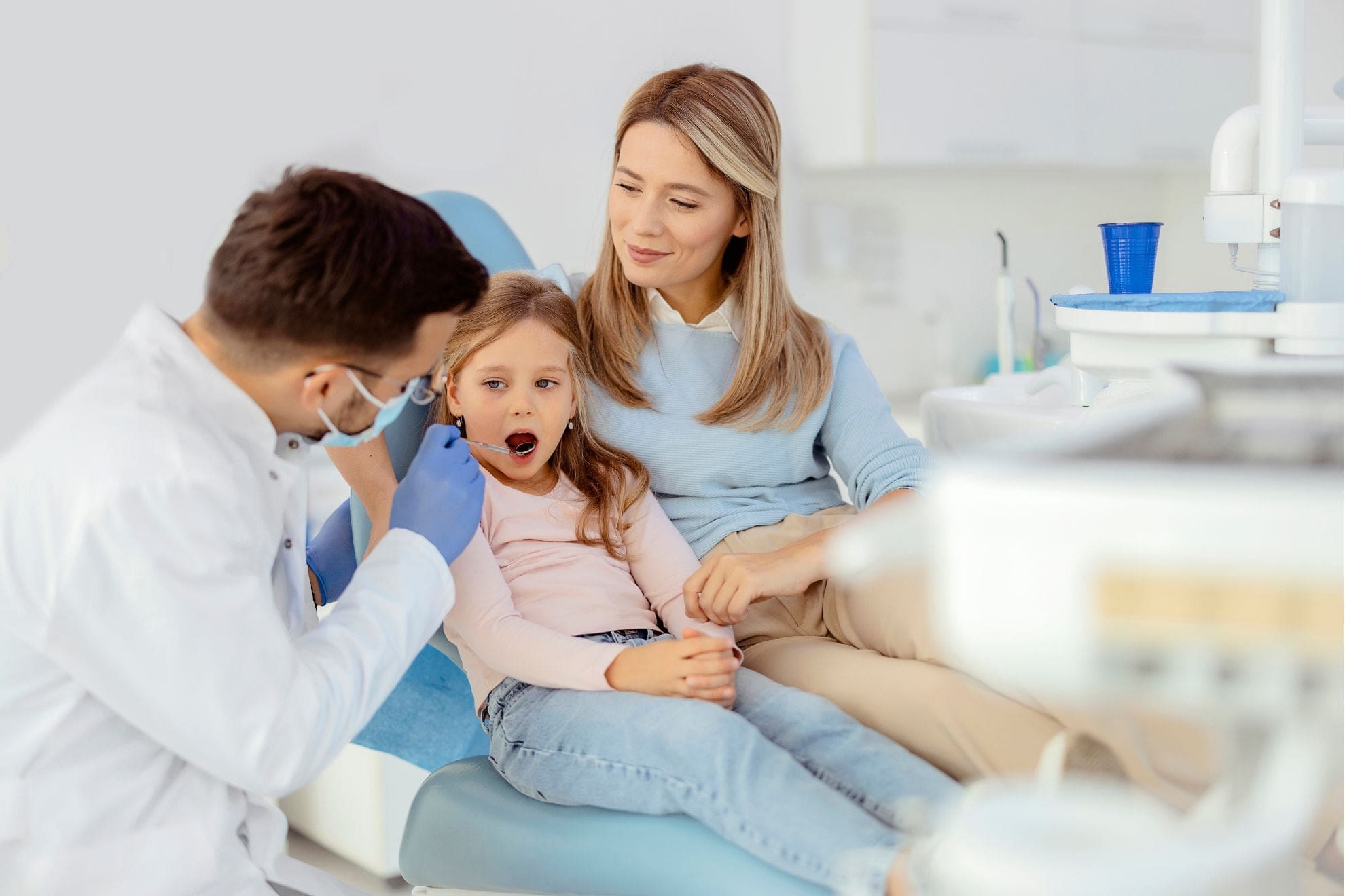At Lake Sammamish Kids Dentistry - Pediatric Dentist in Sammamish WA, a dentist provides safe and precise care for children from infants to teens, examining a young girl while she sits on her mother's lap.