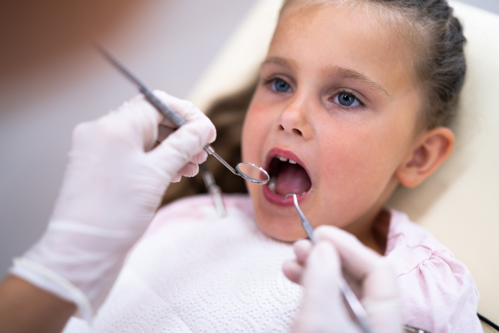 At Lake Sammamish Kids Dentistry - Pediatric Dentist in Sammamish, WA, a child sits in a dental chair with their mouth open as a gloved dentist examines their teeth using dental instruments as one of the procedures of Pediatric Dental Emergencies in Sammamish, WA..