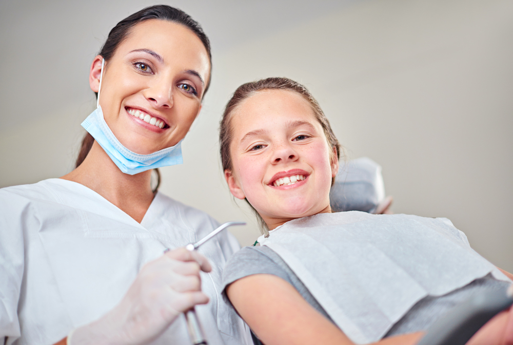 At Lake Sammamish Kids Dentistry - Pediatric Dentist in Sammamish, WA, a dentist wearing gloves and a mask stands beside a smiling child in the dental chair, both facing the camera in an Autism-Friendly Dental Care in Sammamish, WA.