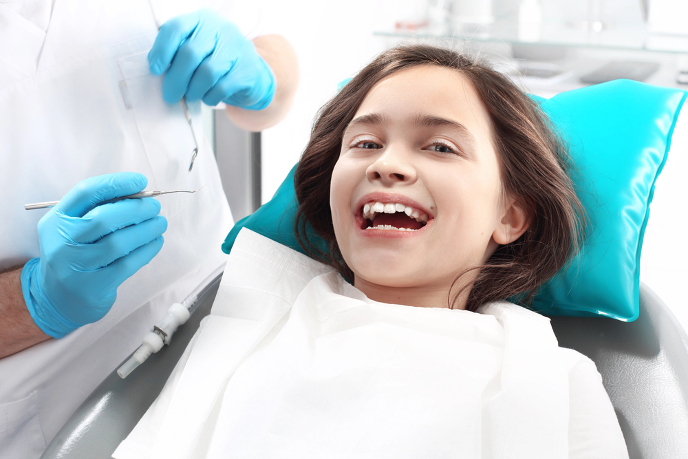 At Lake Sammamish Kids Dentistry - Pediatric Dentist in Sammamish, WA, a young girl smiles in the dental chair as her dentist prepares with tools—reminding parents to ask: When should your child see a dentist in Sammamish, WA?.