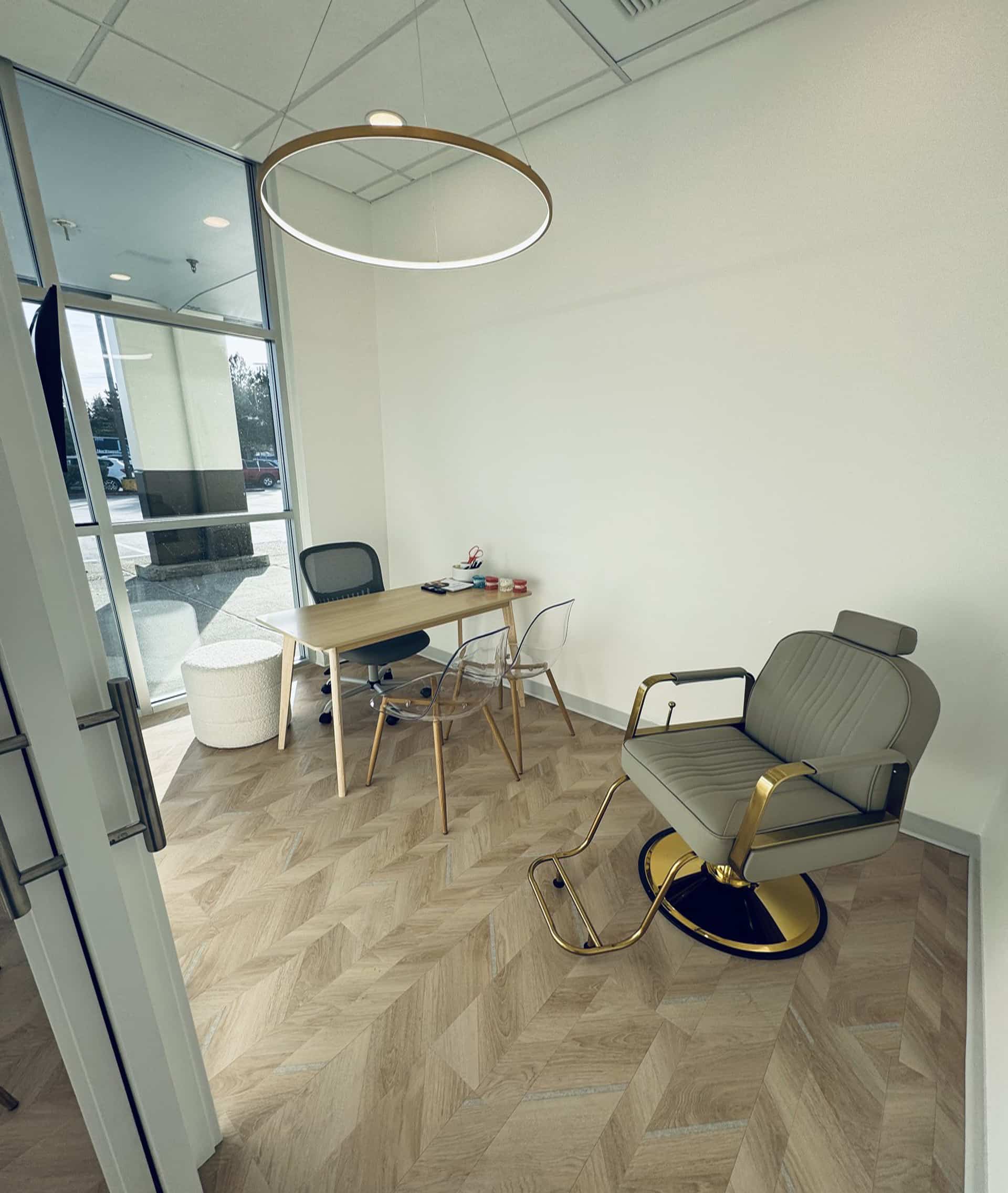 At Lake Sammamish Kids Dentistry - Pediatric Dentist in Sammamish, WA, the office features a wooden desk, two chairs, a gold and gray salon chair, and a circular ceiling light. Large windows fill the space with natural light, creating a warm and welcoming environment for children’s dental consultations.