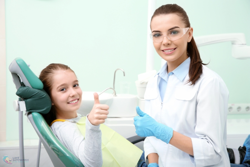 A smiling girl gives a thumbs up in a dental chair with her dentist at Lake Sammamish Kids Dentistry in Sammamish, WA - School Dental Health Programs in Sammamish, WA