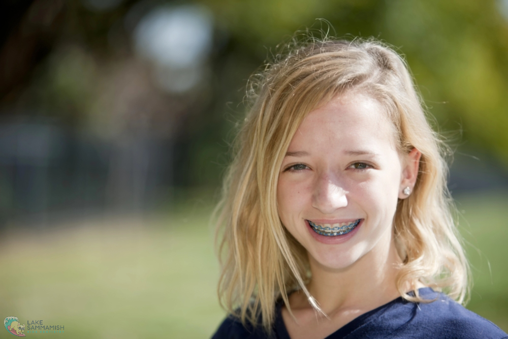 Smiling blonde youth with braces outdoors at Lake Sammamish Kids Dentistry in Sammamish, WA, green background blurred - Tooth-Friendly Snacks for Kids: Dentist Recommendations from Sammamish, WA 